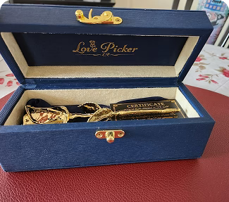 Blue box with 'Love Picker' branding containing a gold-dipped rose and a certificate on a red surface.