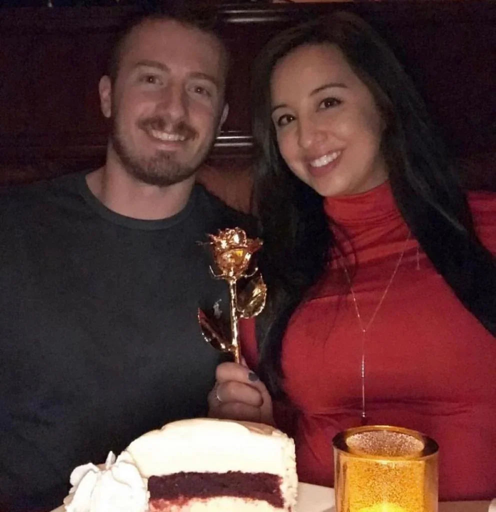 Woman holding 24K gold dipped rose with couple celebrating anniversary, cake and candlelight