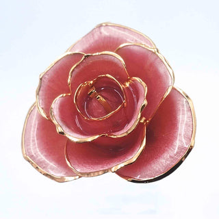 A rose-shaped brooch featuring glossy pink petals with polished gold-tone metallic edges, shown on a plain light background.
