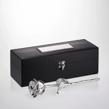 Silver preserved rose with natural stem and leaves displayed in front of black textured gift box