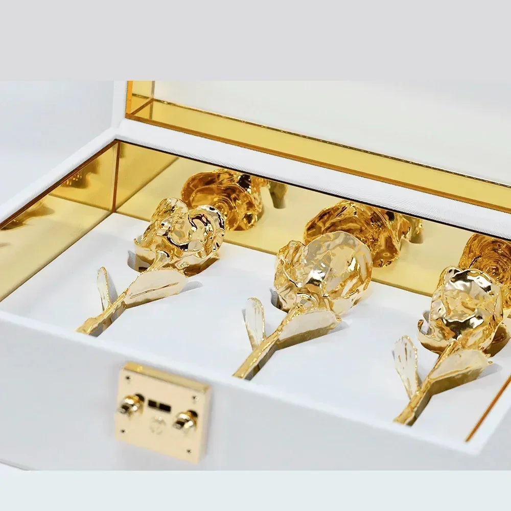 Three gold dipped roses displayed in a white acrylic chest with gold accents.