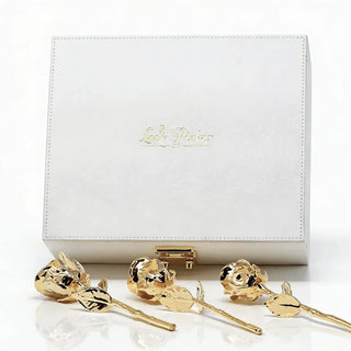 Three gold-dipped preserved roses displayed in front of a white gift box with gold details. Lovepicker 